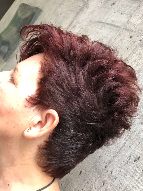 Person with short, textured dark red hair styled in layers, viewed from the side against a concrete background.