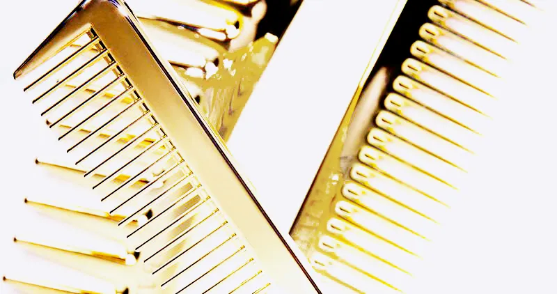 Close-up of two gold metal combs crossing against a white background. The image focuses on the combs' teeth, emphasizing their reflective surface and metallic sheen.