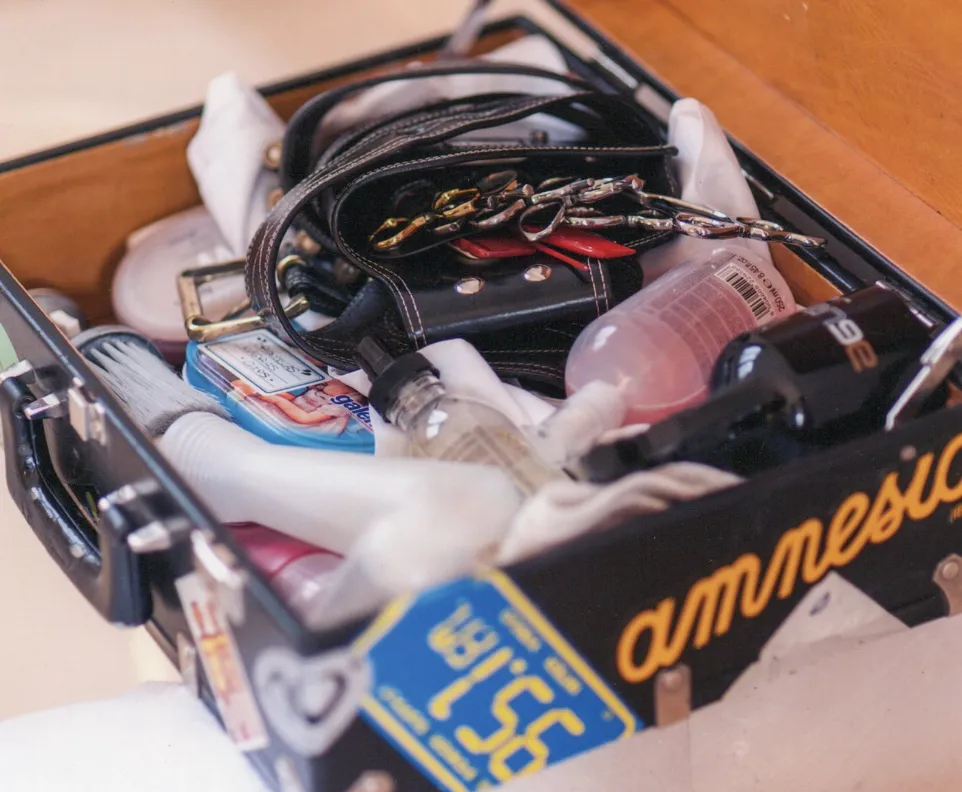 An open suitcase filled with various items including a bottle, a brush, a small cleaning spray, a keychain with multiple keys, a small leather bag, and a towel. The outside of the suitcase is decorated with stickers.