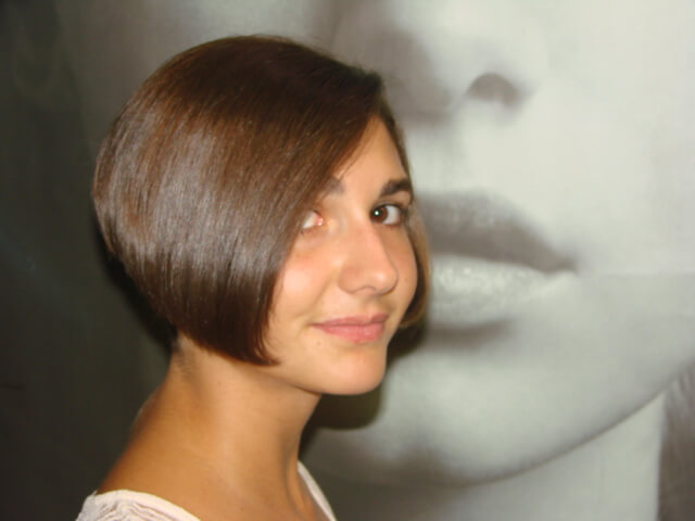 A person with short, sleek brown hair smiles softly, looking to the side. The background features a large, blurred grayscale image of a woman's face.